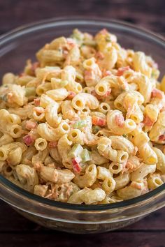 a glass bowl filled with macaroni salad on top of a wooden table next to a fork