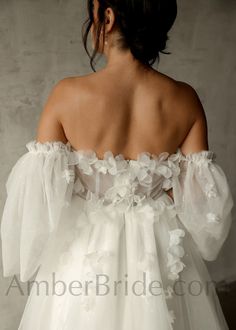 the back of a woman's white wedding dress with flowers on her shoulder and sleeves