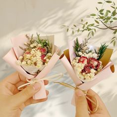 two hands holding small bouquets with strawberries and other flowers in them on a table