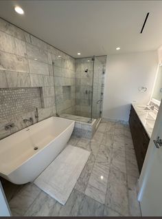 a large bathroom with marble tile flooring and white bathtub next to double sinks