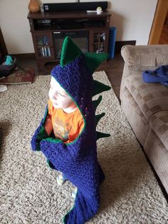 a small child in a crocheted dinosaur costume on the floor next to a couch