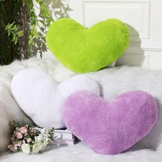 two heart shaped pillows sitting next to each other on a white fur covered bed with flowers