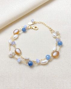 This beautiful layered bracelet showcases a stunning mix of blue and copper gems. The bold mix of gems creates a unique and eye-catching design, while the addition of smooth and baroque pearls adds a touch of elegance. With an adjustable lobster clasp and extender chain, this bracelet offers a perfect fit for anyone looking to make a statement.  Length: 7 inches plus 1-inch extender Materials: gold fill, kyanite, blue lace agate, cultured freshwater pearls, copper moonstone Gift box included. Blue Moonstone Beaded Bracelets With Gemstone Beads, Handmade Blue Moonstone Beaded Bracelets, Blue Double Strand Bracelets As Gift, Blue Moonstone Beaded Bracelets Gift, Handmade Blue Moonstone Bracelets, Gift Blue Moonstone Beaded Bracelets, Blue Moonstone Bracelets For Healing, Blue Moonstone Bracelet For Healing, Spiritual Blue Moonstone Bracelets