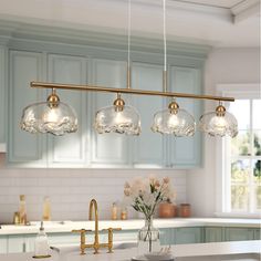 three lights hanging over a kitchen island with flowers in vases on the counter top