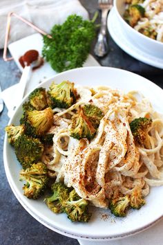 a white bowl filled with pasta and broccoli on top of a table next to silverware