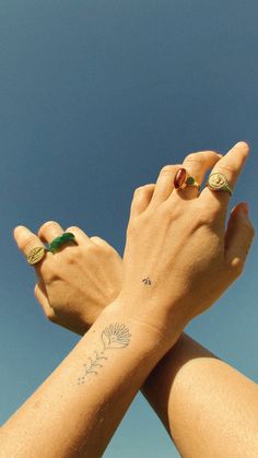 two hands are holding each other with tattoos on their wrists and fingers, against a blue sky