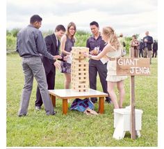 a group of people standing around a giant wooden block tower on top of a grass covered field