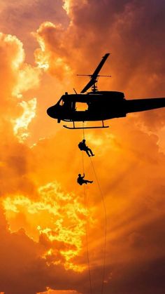 a helicopter is being lowered into the air by two people in front of an orange and yellow sky