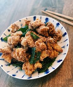 a white plate topped with fried food next to chopsticks on a wooden table