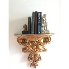 an ornate shelf with books and statues on it against a white wall in the corner