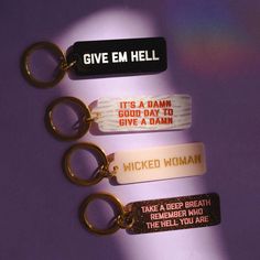 three keychains with different sayings on them sitting next to each other in front of a purple background