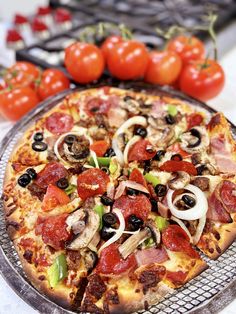 a pizza sitting on top of a metal pan covered in toppings next to tomatoes