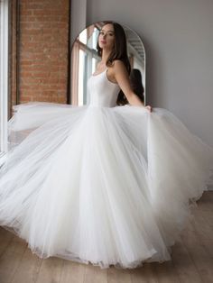 a woman in a white dress is standing near a window and looking into the distance