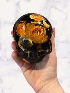 a hand holding a black glass vase with yellow flowers in it on a marble surface