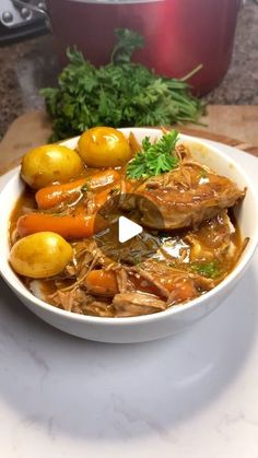 a white bowl filled with meat and vegetables on top of a table next to a pot