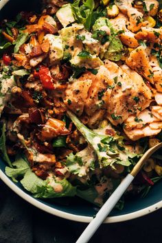 a salad with chicken, lettuce and tomatoes in a bowl next to a fork