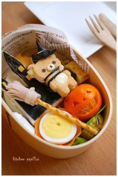 a plastic container filled with halloween food on top of a wooden table next to utensils