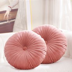 two pink pillows sitting on top of a white couch next to a painting and piano