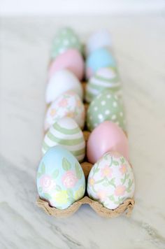 an egg carton filled with painted eggs on top of a marble countertop in pastel colors