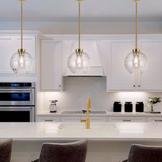 three lights hanging from the ceiling in a kitchen with white cabinets and marble counter tops