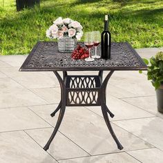 an outdoor table with wine glasses and flowers on it, next to a potted plant