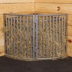 a metal gate with hay in it on top of a black floor next to wooden walls