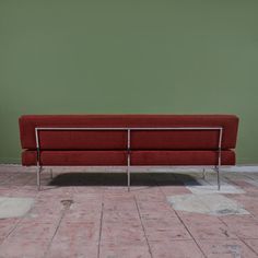 a long red couch sitting on top of a tiled floor next to a green wall