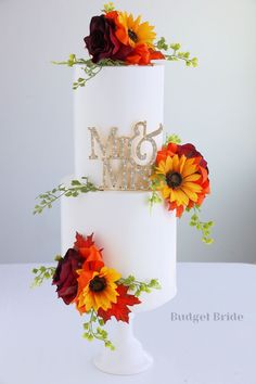 a three tiered white wedding cake with sunflowers and greenery on top