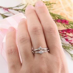 a woman's hand with a diamond ring on top of her finger and flowers in the background