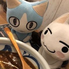 two stuffed animals are sitting next to a bowl of food and a spoon in front of them