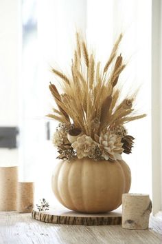 a white pumpkin decorated with dried flowers and feathers sits on a table next to a cork board