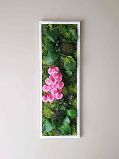 an arrangement of pink flowers and green plants on a white wall above a black chair