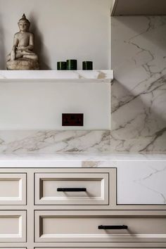 a kitchen with marble counter tops and white cabinetry, along with a buddha statue