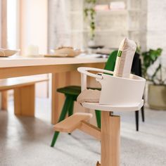 a white high chair sitting on top of a wooden table next to a green chair