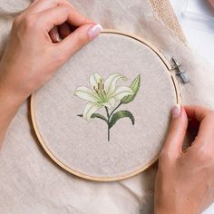 a woman is holding a cross - stitch hoop with a white flower in the center