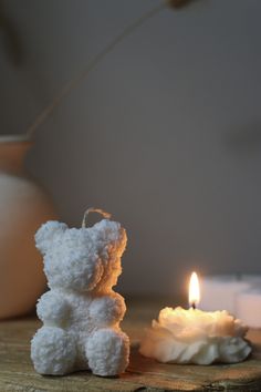 a white teddy bear sitting next to a lit candle