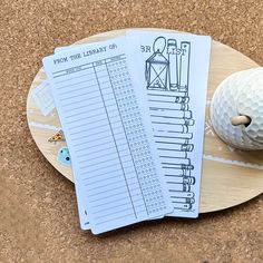 two paper bills sitting on top of a wooden plate next to a golf ball and tee