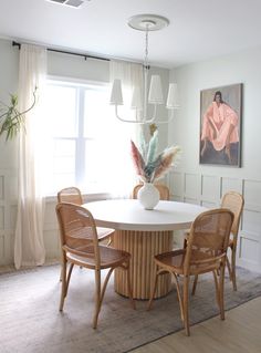 a dining room table with four chairs and a vase on top of it in front of a window