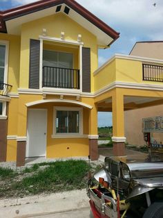 a car is parked in front of a yellow two story house with balconies