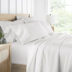 a bed with white sheets and pillows next to a night stand on a wooden table