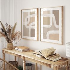 two framed pictures hang on the wall above a wooden table with books and vases