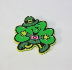 a green shamrock with a pink bow tie on it's lap and wearing a hat