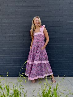 Meet Maisie, our newest cotton block print maxi dress in a Pink Posey print! She's full of sweet details like a tiered skirt, and contrasting striped banding. The bow straps are adjustable for the perfect fit, and it features a smocked back panel for comfort. Did we mention it has POCKETS!? Whether you're sipping lemonade on the porch or hitting up a summer wedding or soirée, this dress is a fun, versatile addition to your closet. Throw it on with sneakers or sandals, it's truly a go anywhere dr Cotton Dress With Tie Straps And Tiered Skirt, Cotton Maxi Dress With Tie Straps, Cotton Tiered Skirt Maxi Dress For Garden Party, Bohemian Cotton Maxi Dress With Tie Straps, Cotton Tiered Maxi Dress For Garden Party, Cotton Maxi Dress With Tiered Skirt For Garden Party, Tiered Cotton Maxi Dress For Garden Party, Cute Church Dresses, Bow Straps