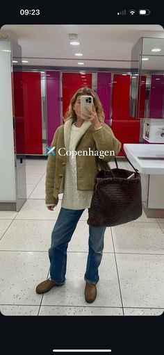 a woman taking a selfie with her cell phone in a public bathroom stall holding a brown purse