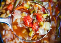 a spoon full of vegetable soup on top of a pan filled with other food items