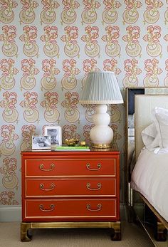 an orange dresser next to a bed with a lamp on top of it and pictures on the side