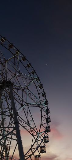 a ferris wheel at dusk with the moon in the sky above it and clouds behind it