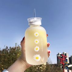 a person holding a bottle with flowers on it in front of some buildings and trees