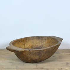 an old wooden bowl sitting on top of a wooden table next to a white wall