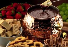 chocolate sauce being poured into a pot with pretzels and strawberries in the background